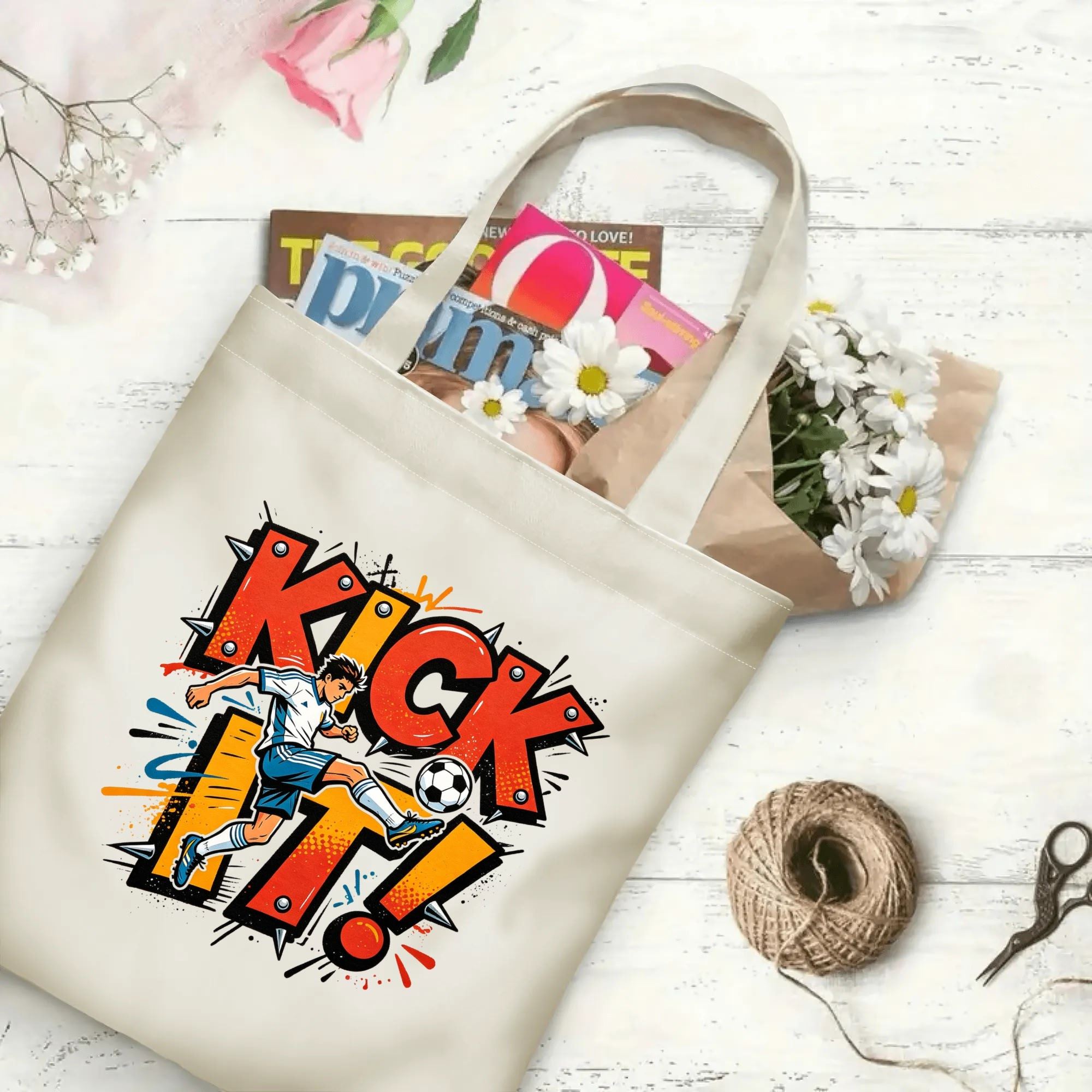 Flat‑lay shot of natural canvas street‑art sports novelty tote bag with bold punk‑style "KICK IT!" typography, dynamic soccer kicker illustration and grunge splash details, decorated with daisies, ideal casual daily‑wear bag for football fans