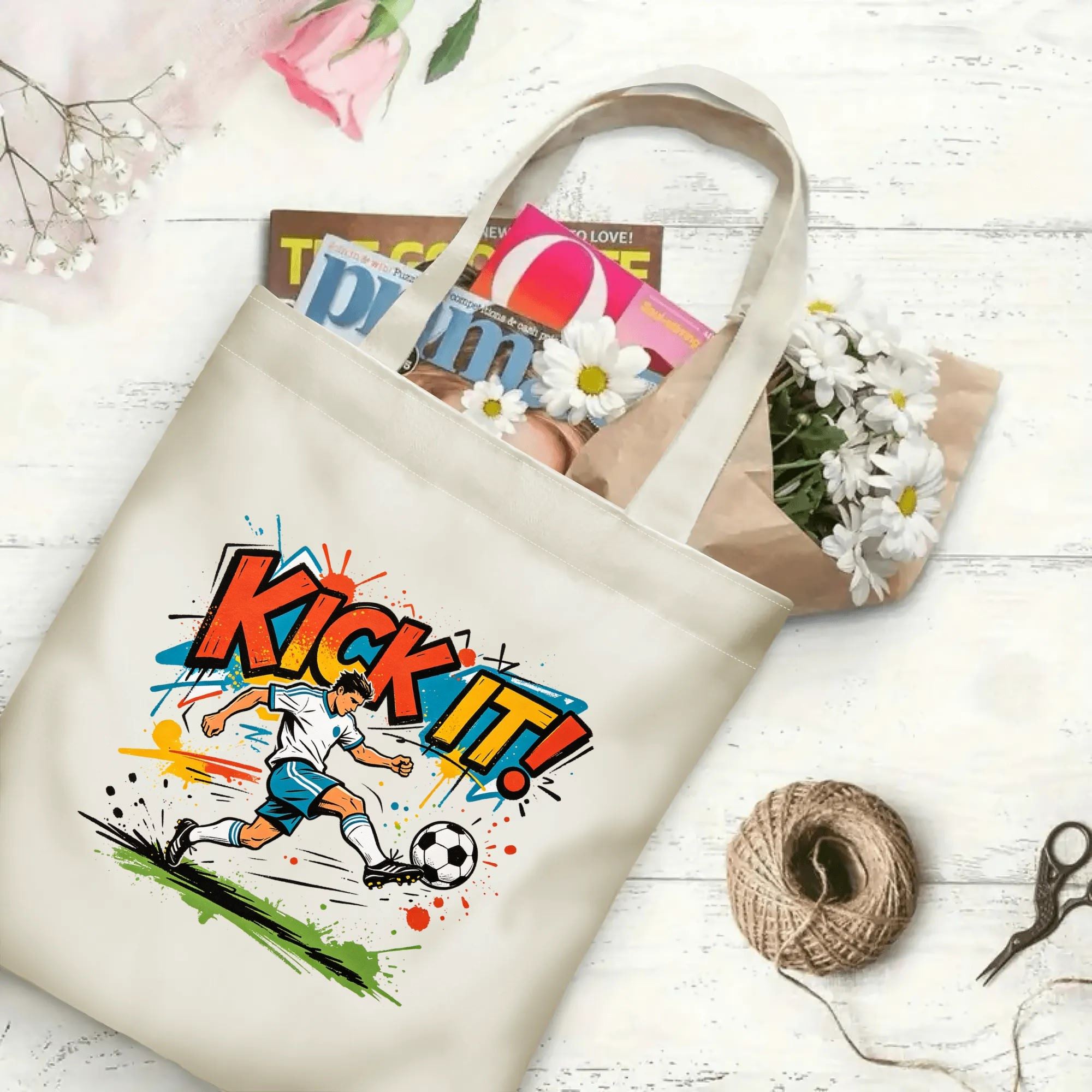 Flat‑lay shot of natural canvas pop‑art sports novelty tote bag with eye‑catching splash‑style "KICK IT!" typography, energetic soccer kicker illustration and grunge color‑burst details, decorated with daisies, ideal casual daily‑wear bag for football fans