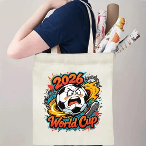 Person carrying natural canvas 2026 World Cup fan‑gift tote bag with bold rebellious punk‑cartoon soccer‑ball design, reusable sports accessory for tournament viewing, fan events or everyday errands