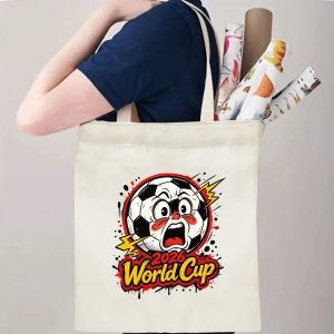 Person carrying natural canvas 2026 World Cup fan‑gift tote bag with bold expressive cartoon soccer‑ball mascot design, reusable sports accessory for tournament viewing, fan events or everyday errands