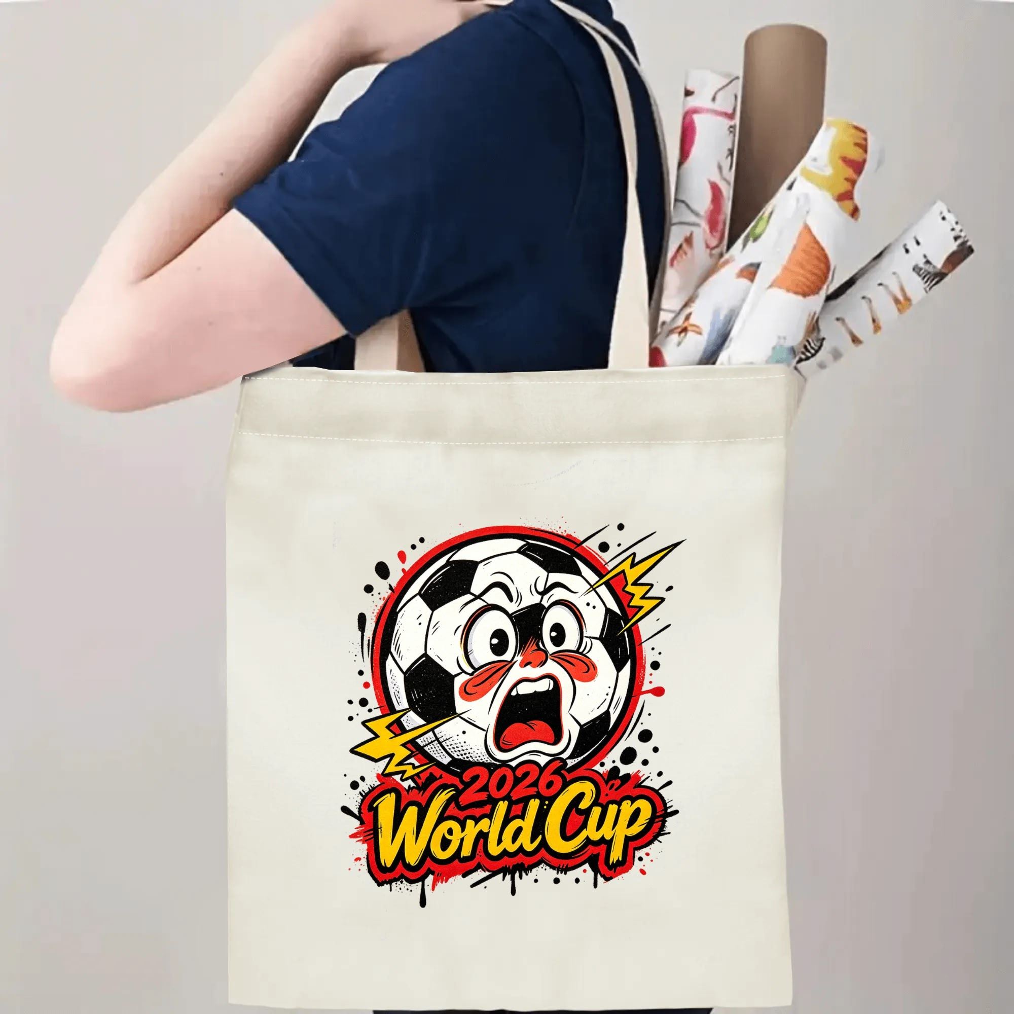 Person carrying natural canvas 2026 World Cup fan‑gift tote bag with bold expressive cartoon soccer‑ball mascot design, reusable sports accessory for tournament viewing, fan events or everyday errands