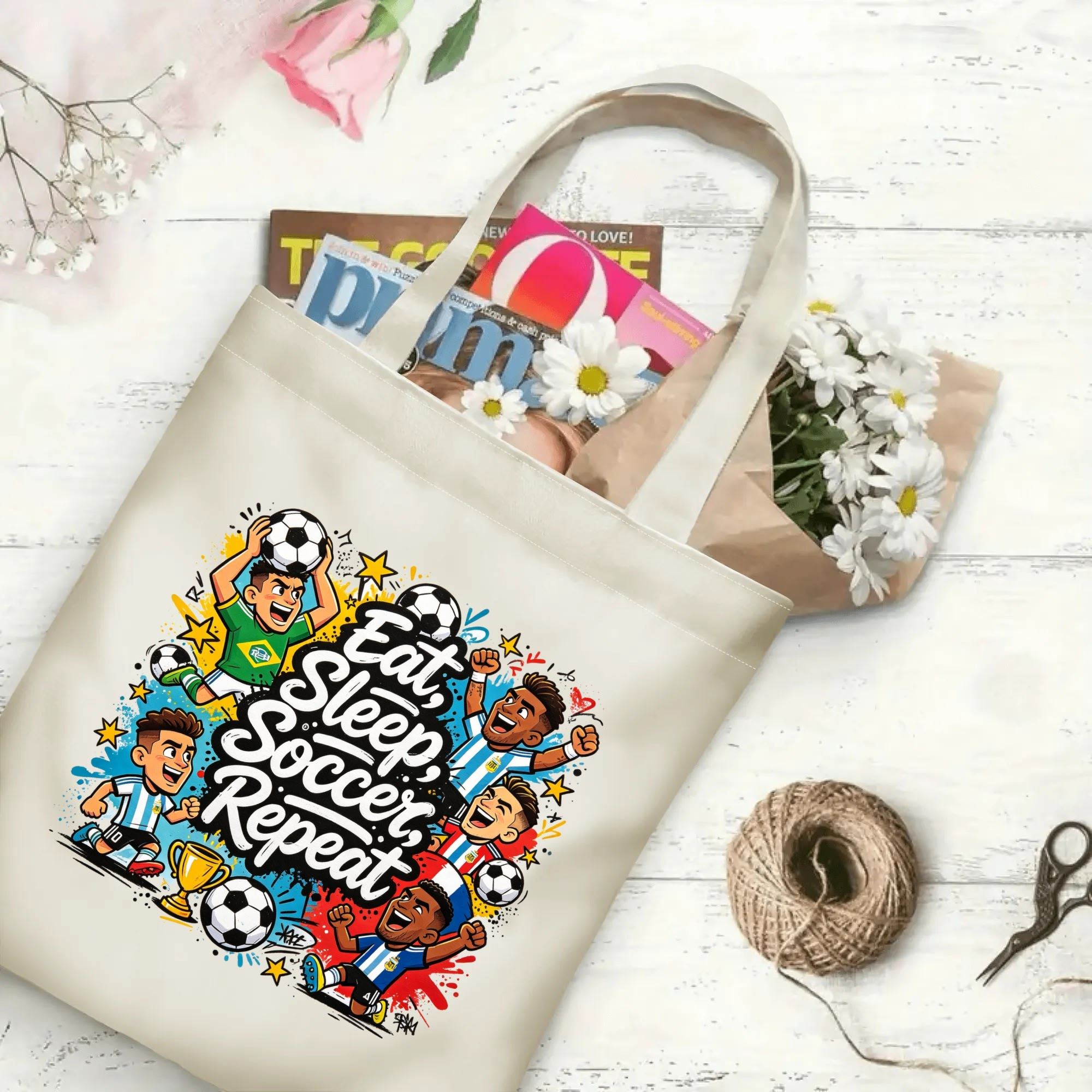 Flat‑lay shot of natural canvas novelty football tote bag with lively international player cartoon graphic, fun soccer lifestyle quote, bright splash‑style details and celebratory trophy accents, decorated with daisies, ideal casual daily‑wear bag for World Cup fans