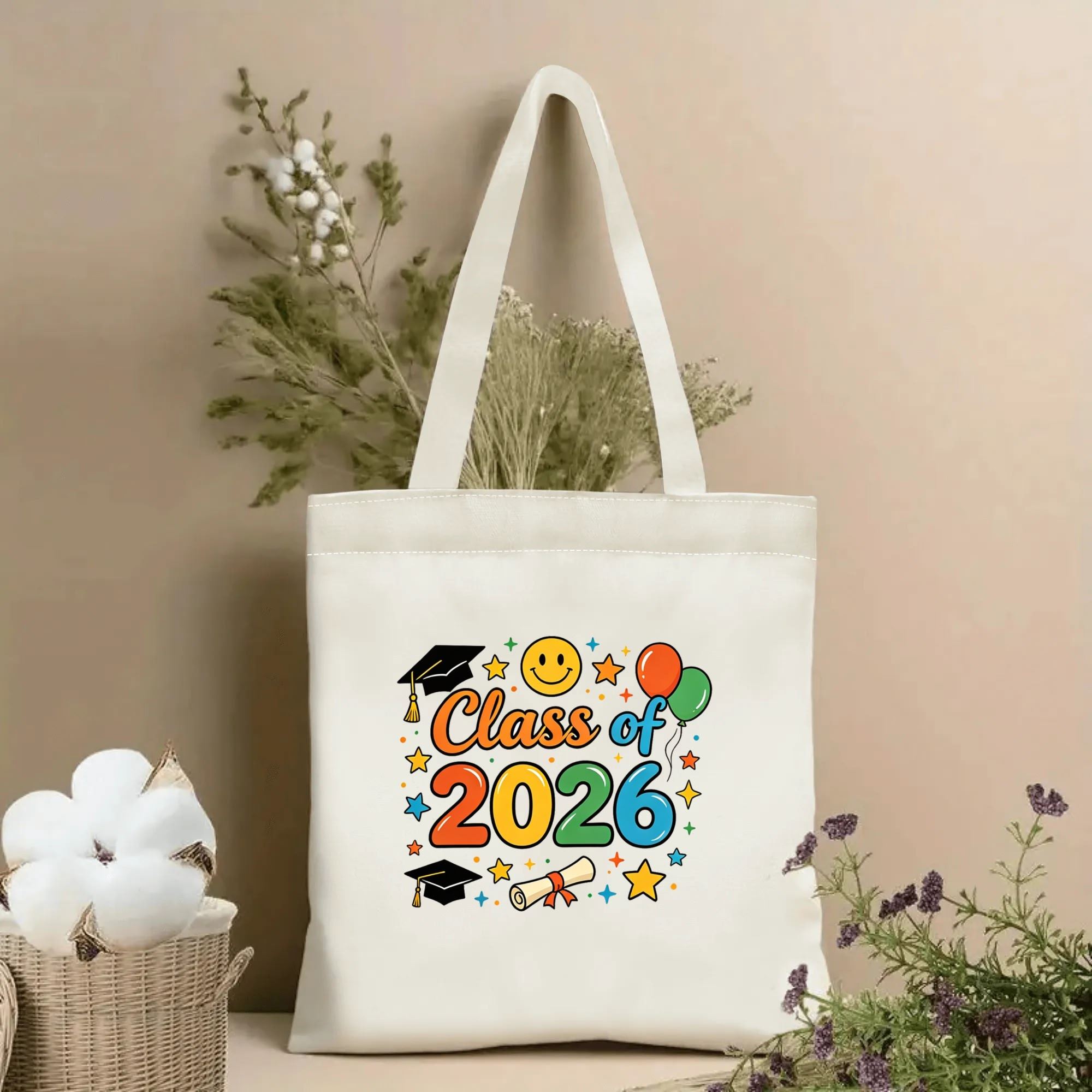 Natural canvas tote bag with colorful "Class of 2026" print, featuring graduation caps, balloons, smiley face, stars, and diploma, graduation-themed design