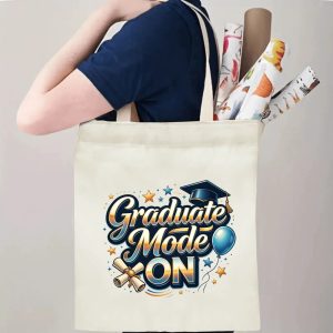 Person carrying a "Graduate Mode ON" canvas tote bag over the shoulder, holding rolled posters and graduation essentials