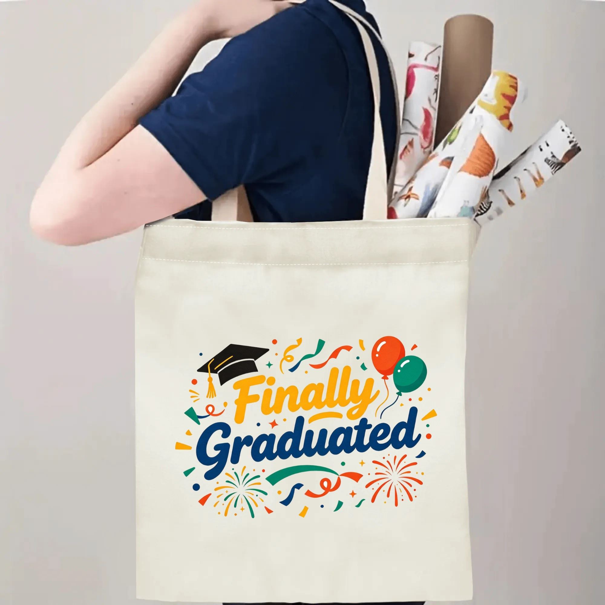 Person carrying a “Finally Graduated” canvas tote bag over the shoulder, with rolled posters and graduation essentials.