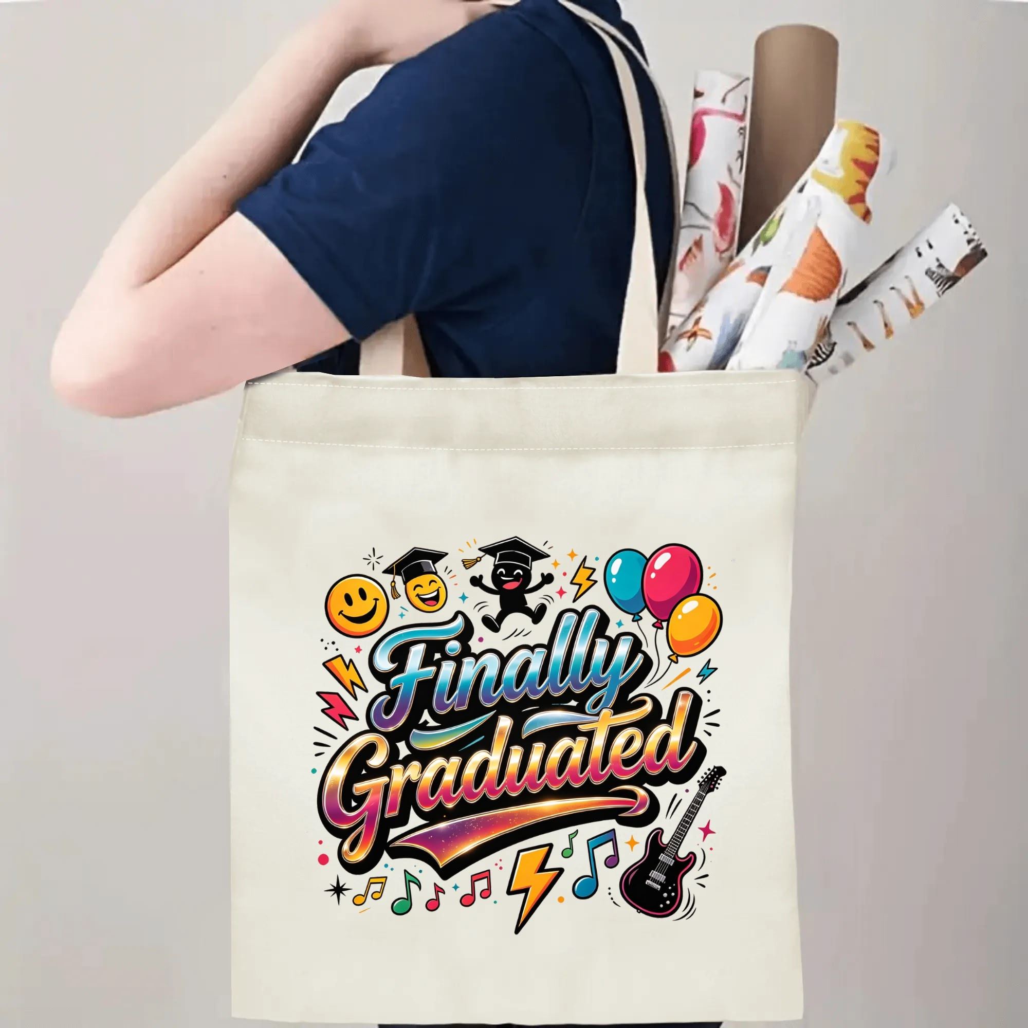Person carrying a canvas tote bag with a colorful “Finally Graduated” print, featuring smiley faces, graduation caps, balloons, music notes, and an electric guitar, over the shoulder with rolled posters.