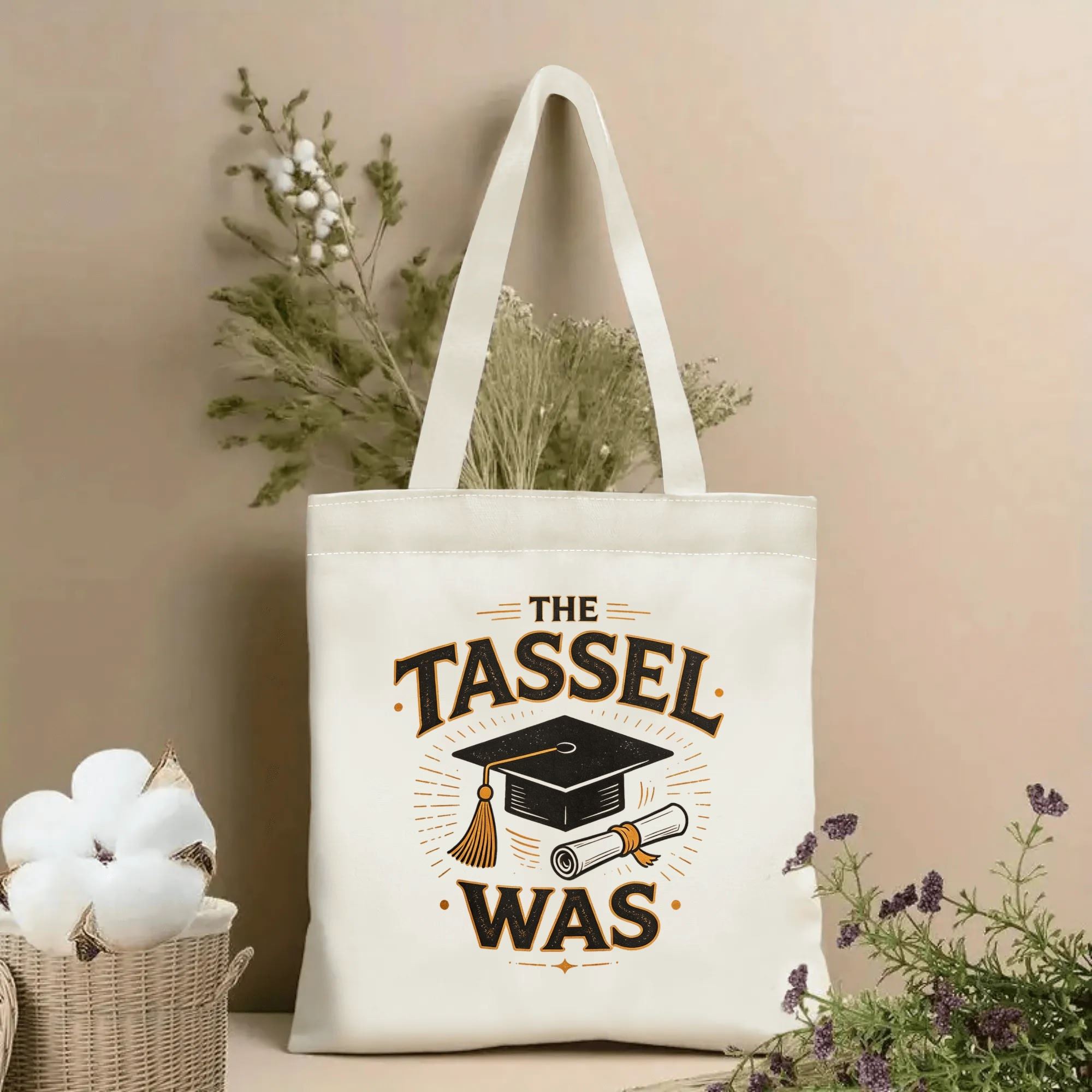 Natural canvas tote bag with “THE TASSEL WAS” print, featuring graduation cap, diploma, and vintage sunburst accents.