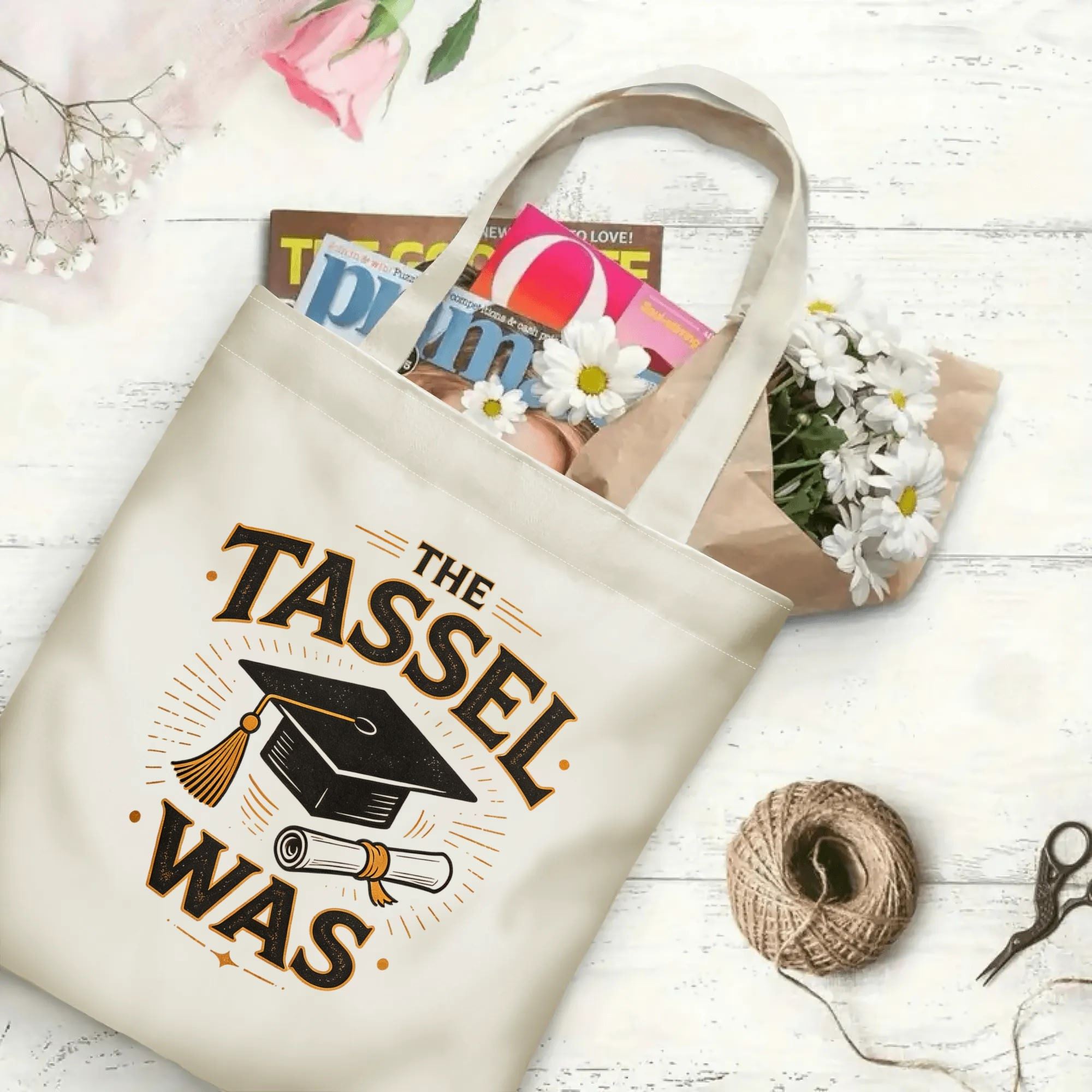 “THE TASSEL WAS” retro‑style canvas tote bag in use, holding books, flowers, and gifts.