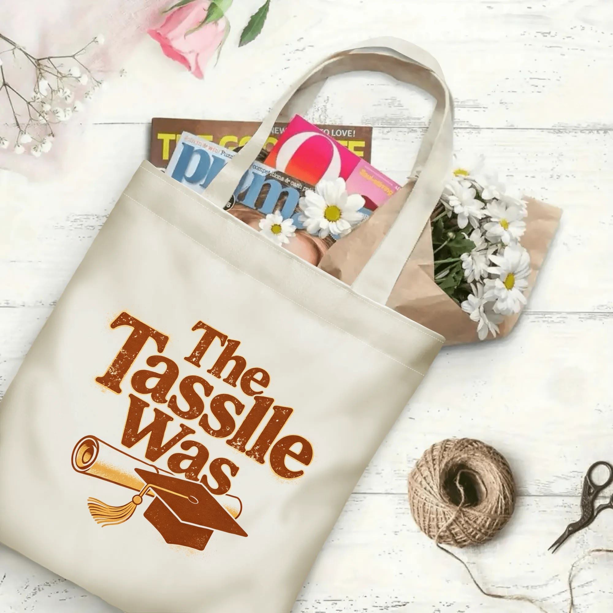 “The Tassle Was” retro canvas tote bag in use, holding books, flowers, and gifts.