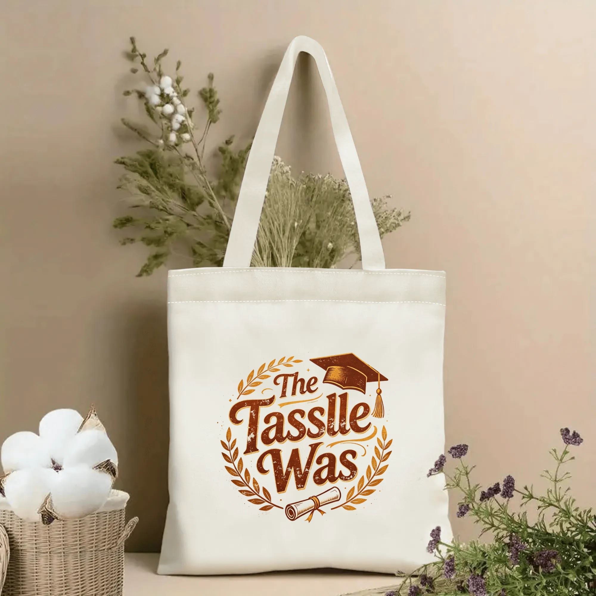 Natural canvas tote bag with “The Tassle Was” print, featuring a laurel wreath, graduation cap, diploma, and distressed vintage text.
