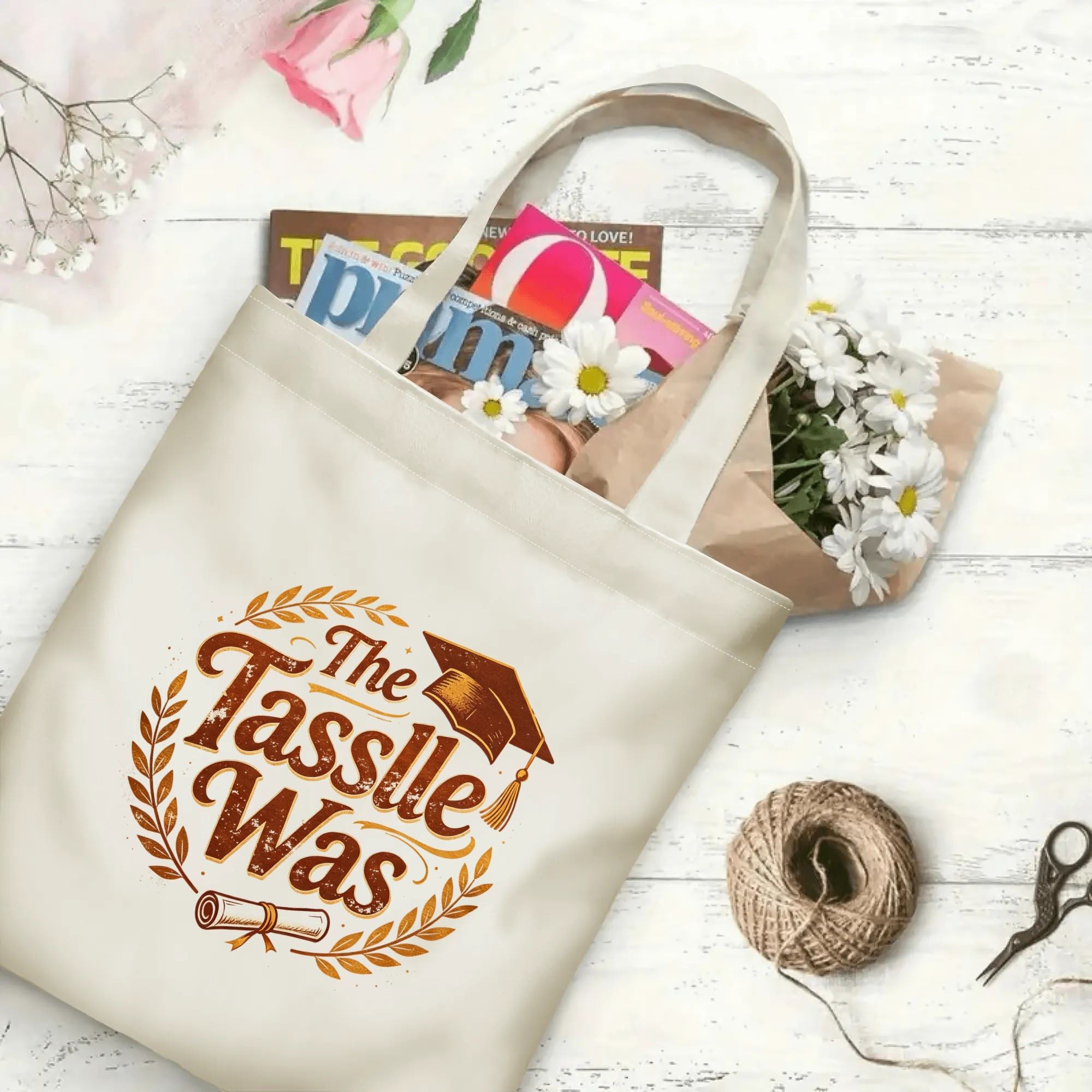 “The Tassle Was” retro‑style canvas tote bag in use, holding books, flowers, and gifts.