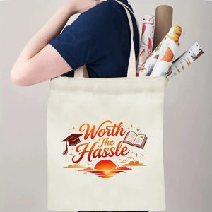 Person carrying a “Worth The Hassle” graduation tote bag over the shoulder, with rolled posters and graduation essentials.