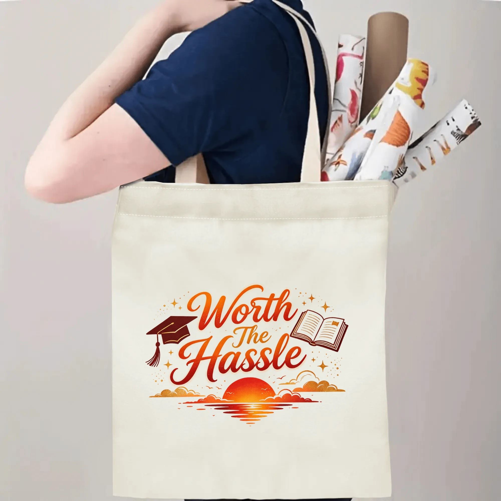 Person carrying a “Worth The Hassle” graduation tote bag over the shoulder, with rolled posters and graduation essentials.