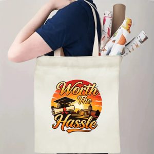 Person carrying a “Worth The Hassle” graduation tote bag over the shoulder, with rolled posters and graduation essentials.