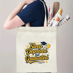 Person carrying a “Sleep Deprived but Graduated” graduation tote bag over the shoulder, with rolled posters and graduation essentials.