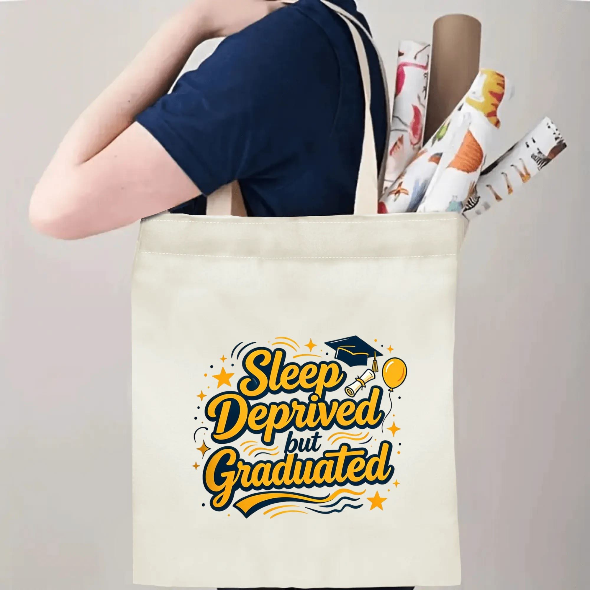 Person carrying a “Sleep Deprived but Graduated” graduation tote bag over the shoulder, with rolled posters and graduation essentials.