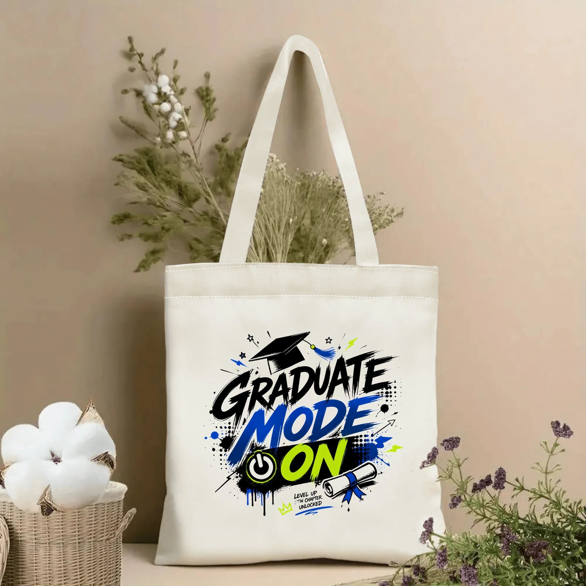 Natural canvas tote bag with “Graduate Mode On” print, featuring a graduation cap, diploma, power button, and graffiti-style accents in black, blue, and neon green.