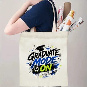 Person carrying a “Graduate Mode On” graduation tote bag over the shoulder, with rolled posters and graduation essentials.