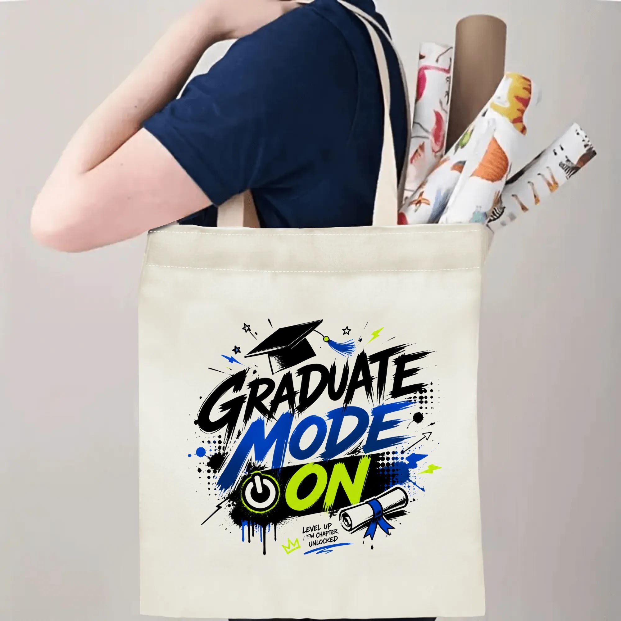 Person carrying a “Graduate Mode On” graduation tote bag over the shoulder, with rolled posters and graduation essentials.