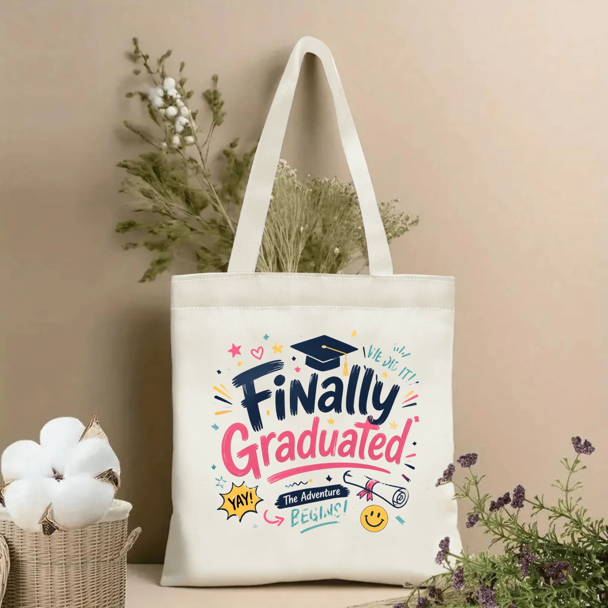 Natural canvas tote bag with “Finally Graduated” print, featuring a graduation cap, diploma, and playful accents like stars, hearts, and smiley faces in bright colors.