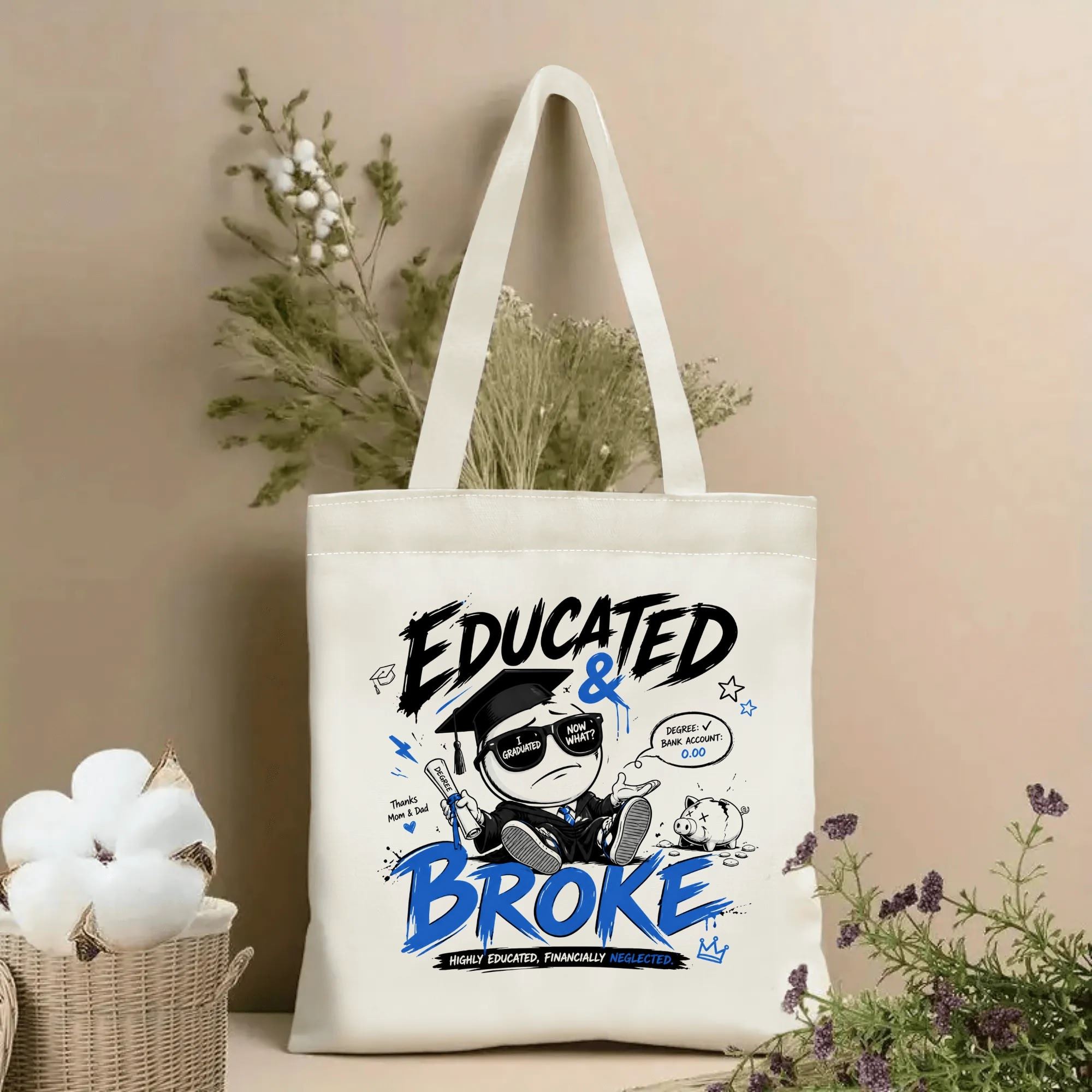 Natural canvas tote bag with “Educated & Broke” print, featuring a humorous cartoon graduate character, graduation cap, diploma, piggy bank, and funny phrases in black and blue.