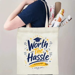 Person carrying a “Worth The Hassle Class of 2026” graduation tote bag over the shoulder, with rolled posters and graduation essentials.