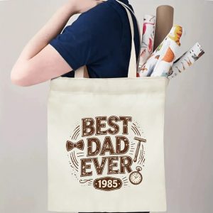 “Best Dad Ever 1985” retro dad-themed canvas tote bag in use, holding groceries, books, and gifts.