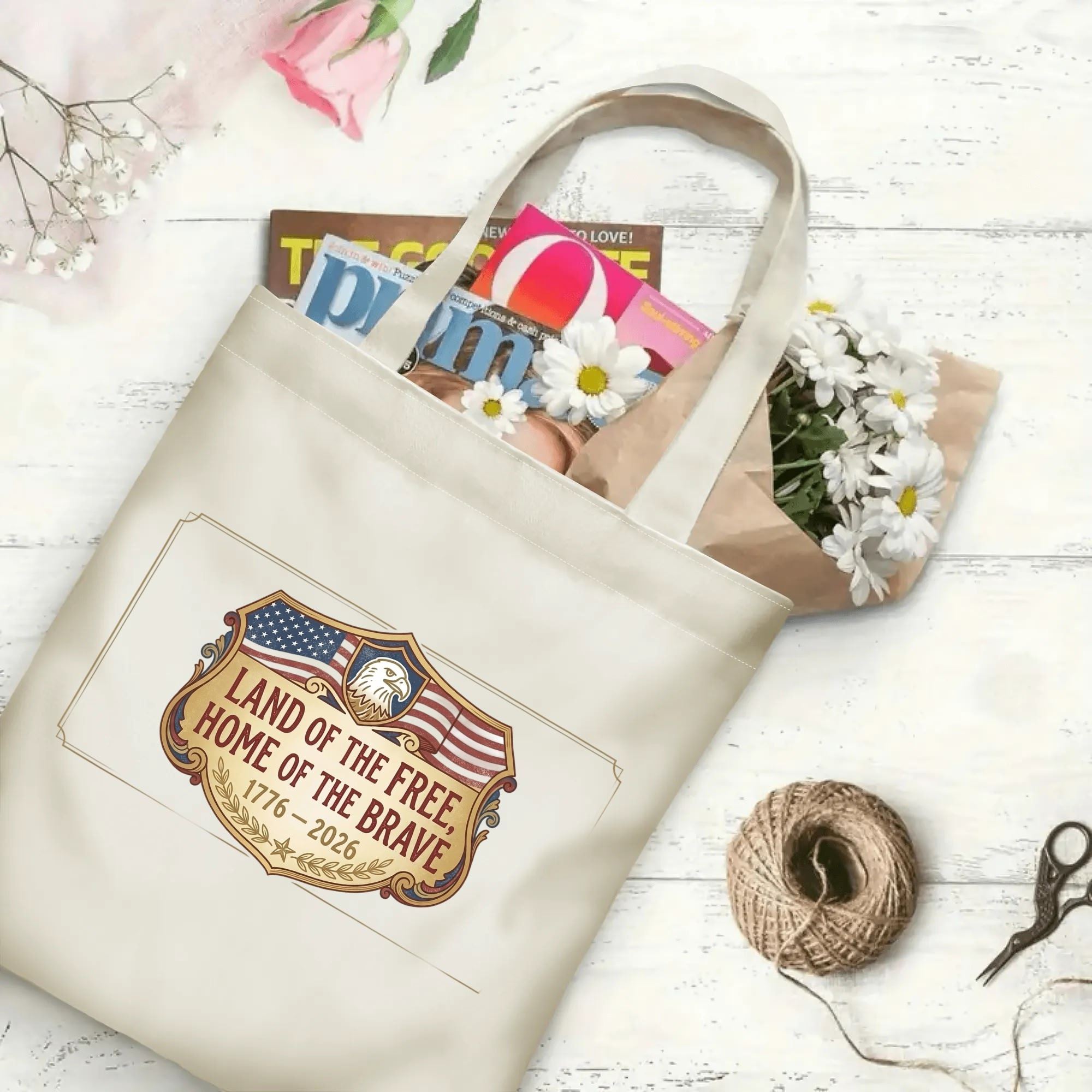 Patriotic shield eagle canvas tote laid flat on wooden table, filled with magazines and fresh flowers to show large storage capacity for daily items.