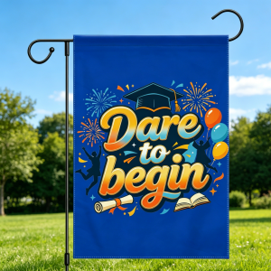 Blue graduation garden flag with "Dare to begin" design, featuring a graduation cap, fireworks, balloons, and silhouettes of celebrating graduates, displayed outdoors on a sunny day.