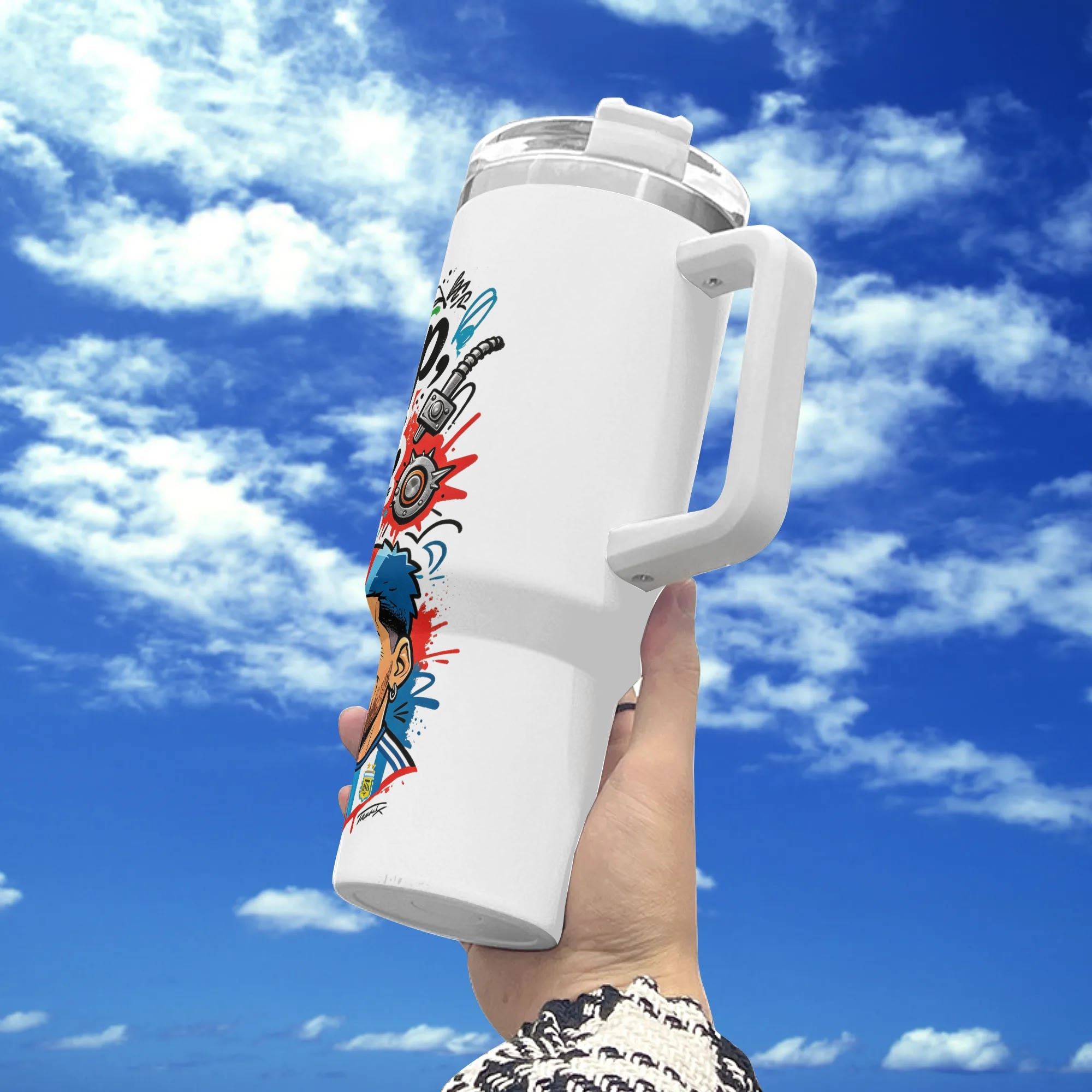 White 40oz insulated stainless steel tumbler with handle, edgy punk‑graffiti blue‑red mohawk Argentina footballer "Eat Sleep Soccer Repeat" print, held against blue sky background, bold street‑style soccer fan travel mug