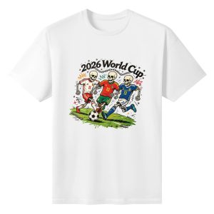 White unisex cotton short‑sleeve t‑shirt, front striking punk‑pop‑art print celebrating the 2026 World Cup, featuring three cartoon skeleton soccer players in national kits competing on grass pitch, rugged chain hardware and bold “2026 World Cup” lettering, edgy goth‑style football‑themed fan tee flat lay