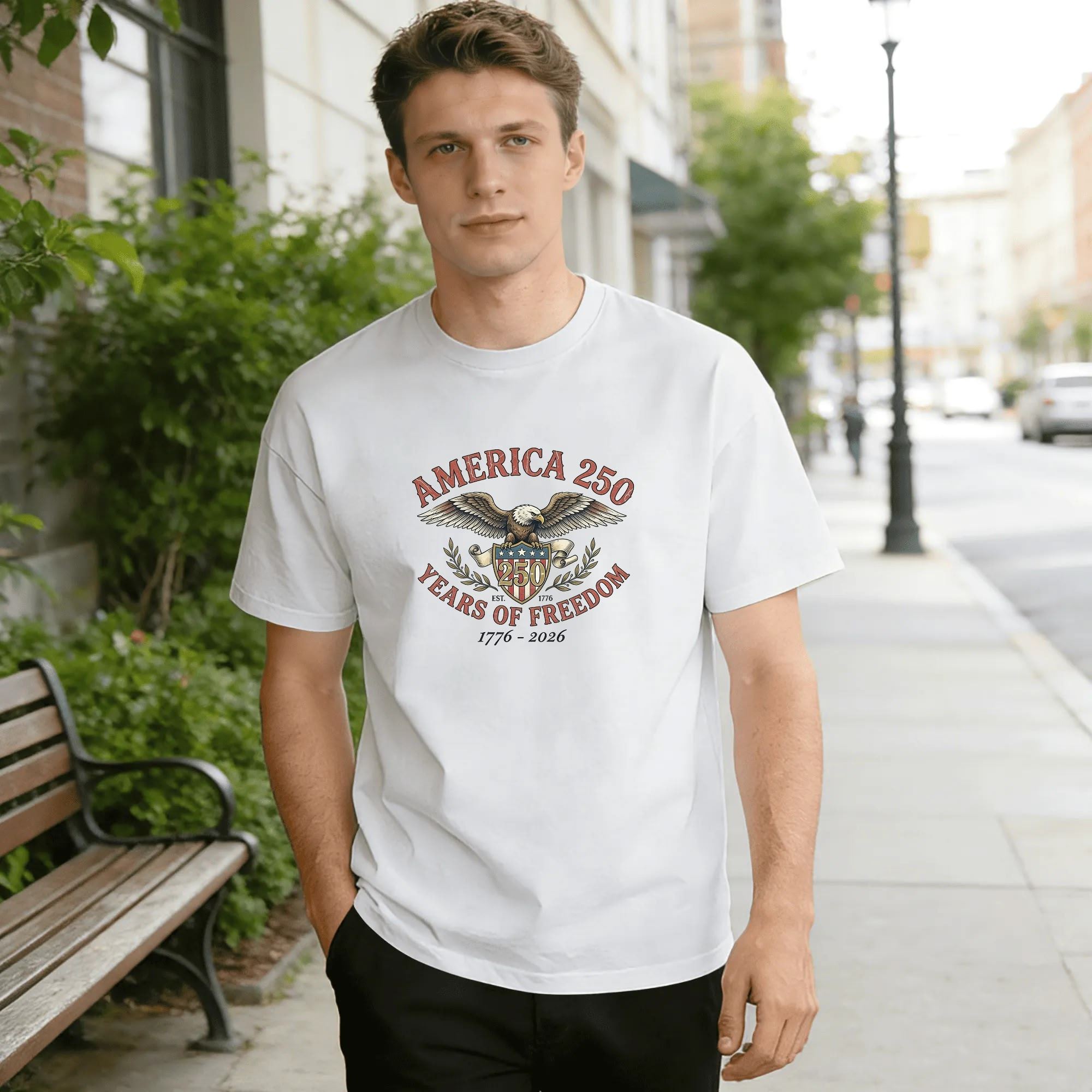 Young man wearing white relaxed‑fit cotton tee with classic vintage patriotic America 250 graphic, majestic bald eagle, American flag shield, laurel wreath, curved text “AMERICA 250 YEARS OF FREEDOM” and founding‑year mark “1776‑2026”, retro‑style outdoor lifestyle shot, timeless USA 250th anniversary commemorative apparel