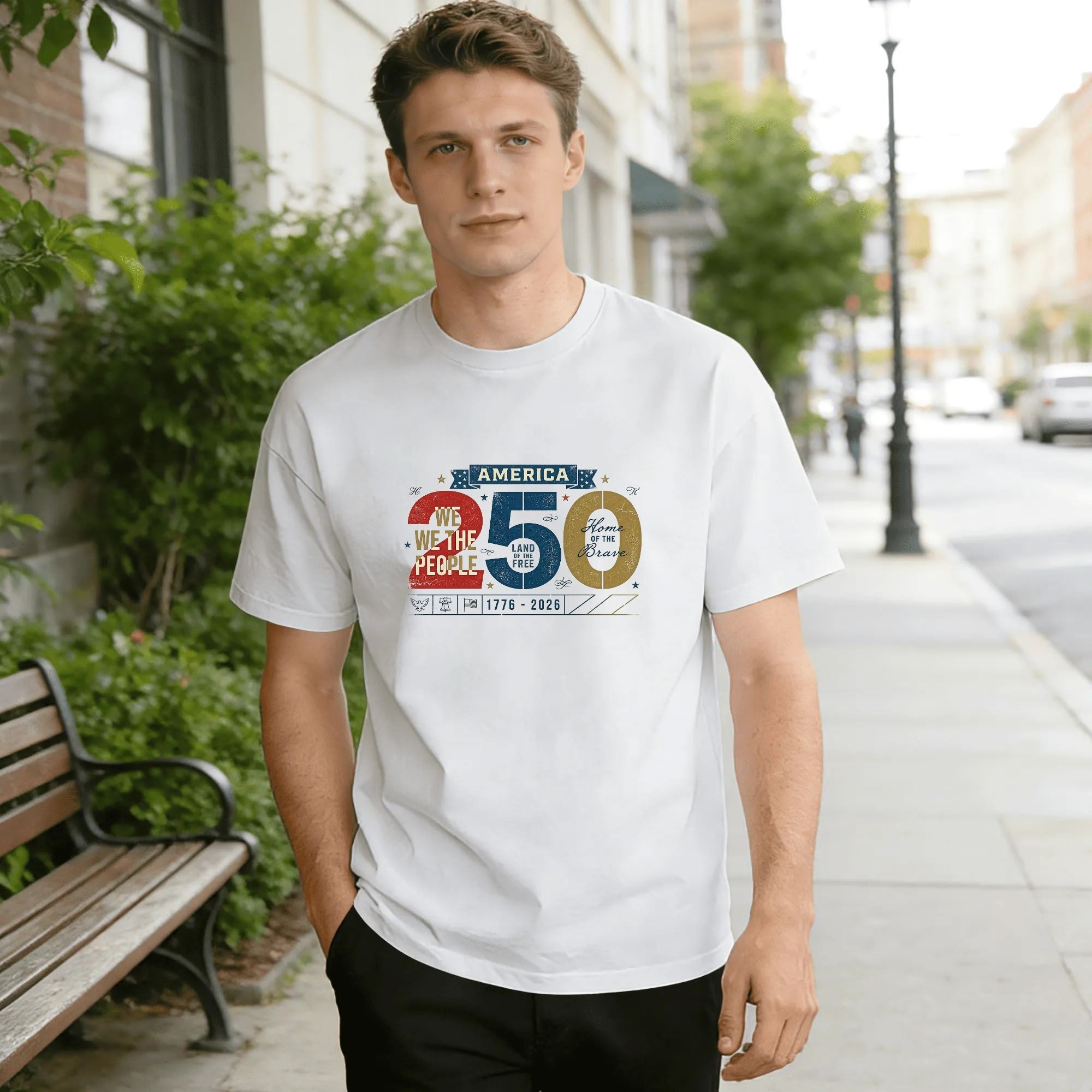 Young man wearing white relaxed‑fit cotton tee with retro distressed America 250 graphic, large split‑color “250” numerals filled with “We the People”, “Land of the Free”, “Home of the Brave”, top banner “AMERICA”, founding year “1776‑2026”, small patriotic eagle‑bell‑flag icons, vintage grunge style, street‑style outdoor lifestyle shot, USA 250th anniversary commemorative apparel