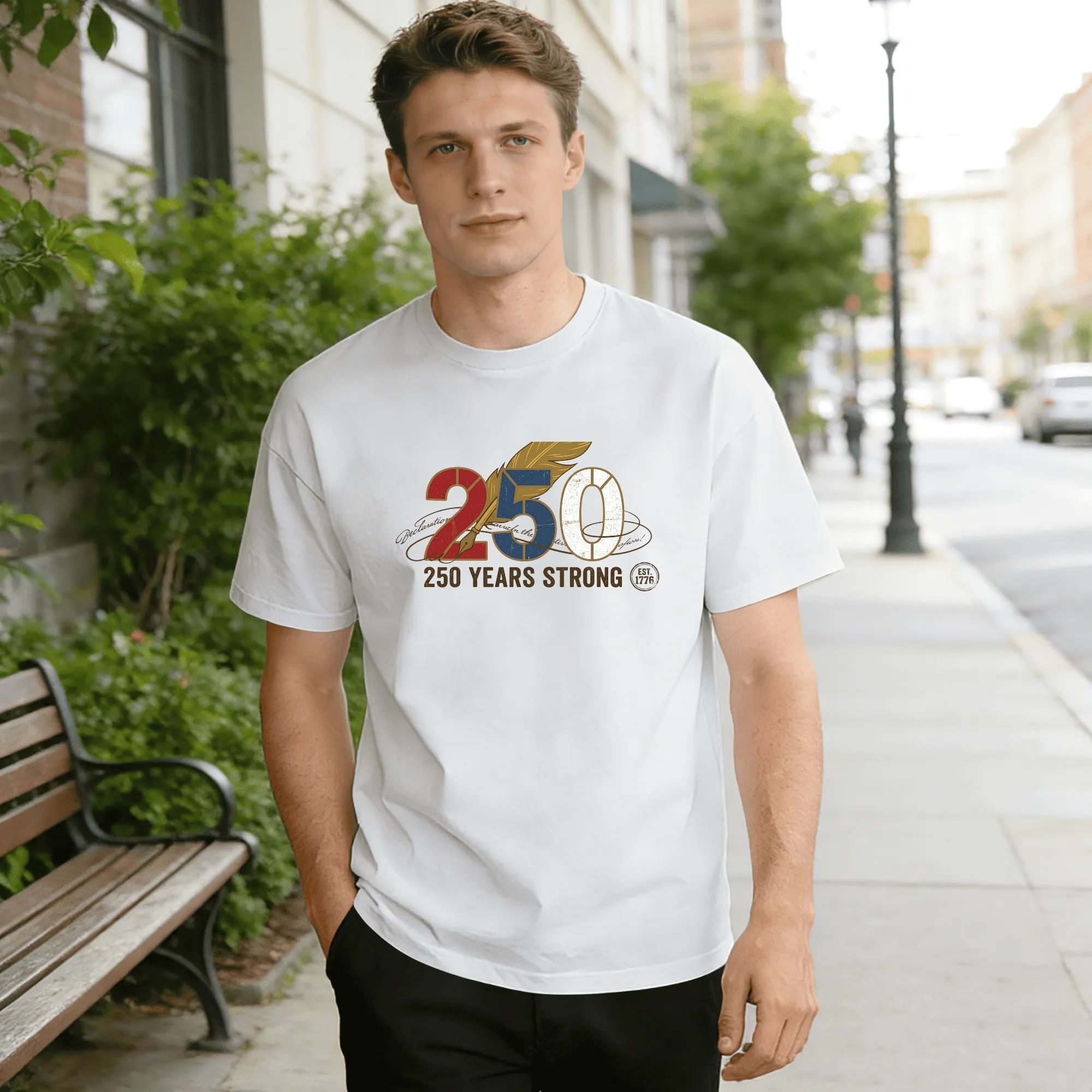 Young man wearing white relaxed‑fit cotton tee with retro patriotic America 250 graphic, stylized red‑blue‑white “250” numerals, golden quill feather, handwritten declaration script, “250 Years Strong” slogan, 1776 founding‑year mark, subtle vintage worn texture, street‑style outdoor lifestyle shot, sleek USA 250th‑anniversary commemorative apparel