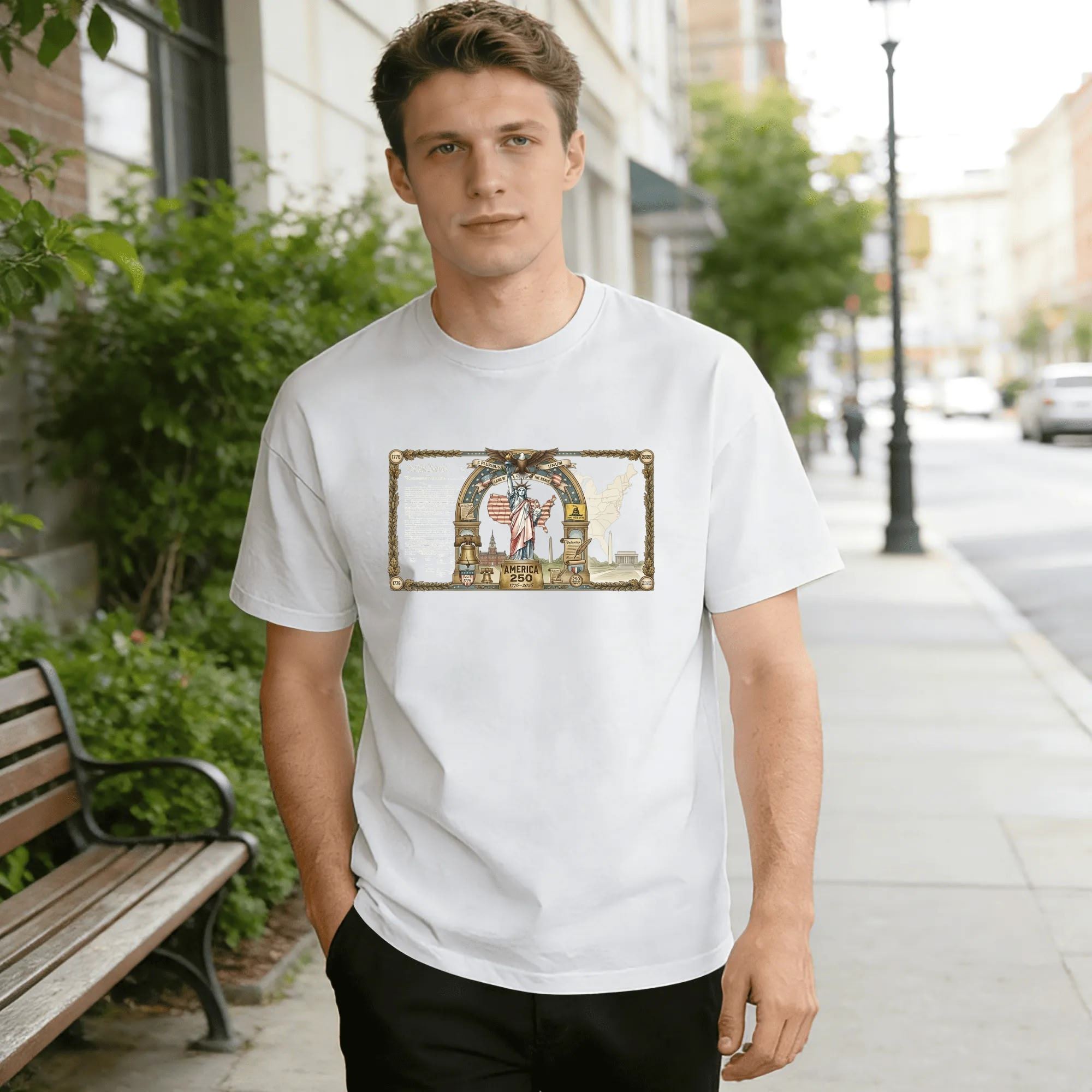 Young man wearing white relaxed‑fit cotton tee with antique framed America 250 graphic, ornate golden‑leaf border, central Statue of Liberty, bald eagle, liberty bell, US map, national landmarks & founding‑document details, vintage currency‑style design, street‑style outdoor lifestyle shot, premium heritage USA 250th‑anniversary commemorative apparel