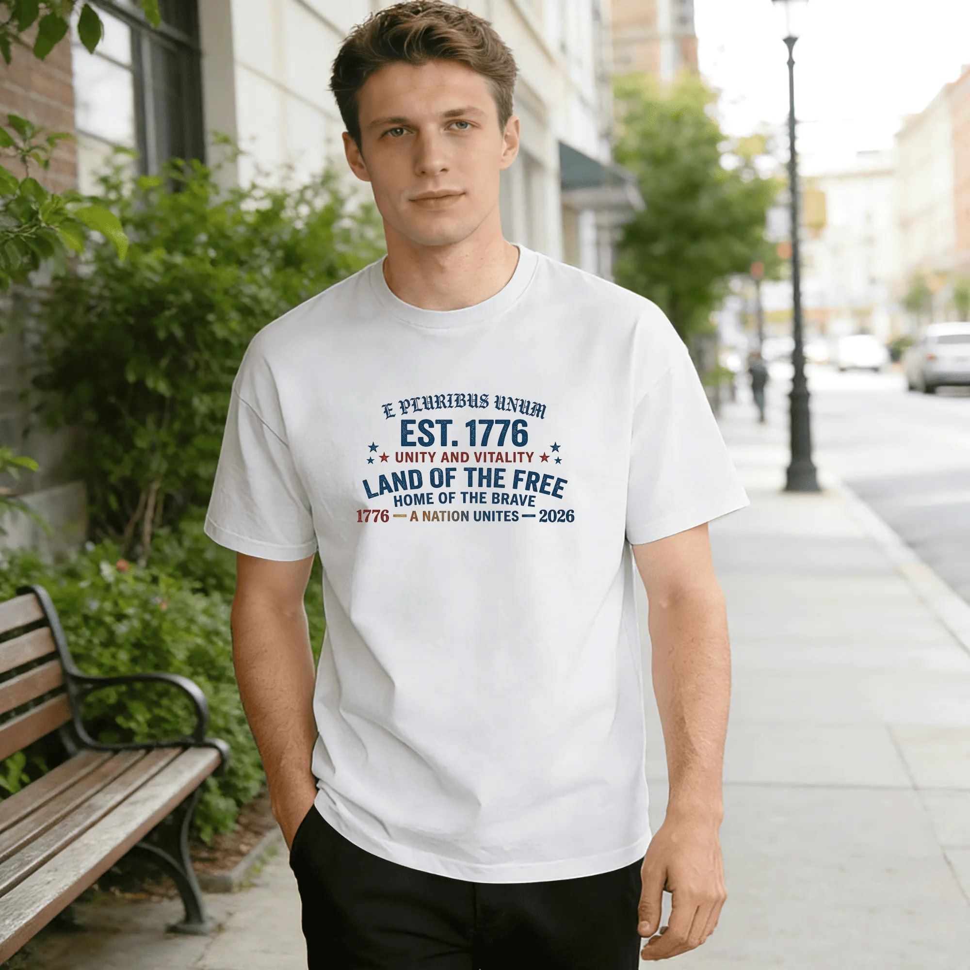 Young man wearing white relaxed‑fit cotton tee with arched vintage America 250 graphic, curved “E Pluribus Unum” script, bold “EST.1776” lettering, patriotic mottos, star accents, 1776‑2026 anniversary dates, distressed red‑white‑blue typography, street‑style outdoor lifestyle shot, classic unity‑themed USA 250th‑anniversary commemorative apparel