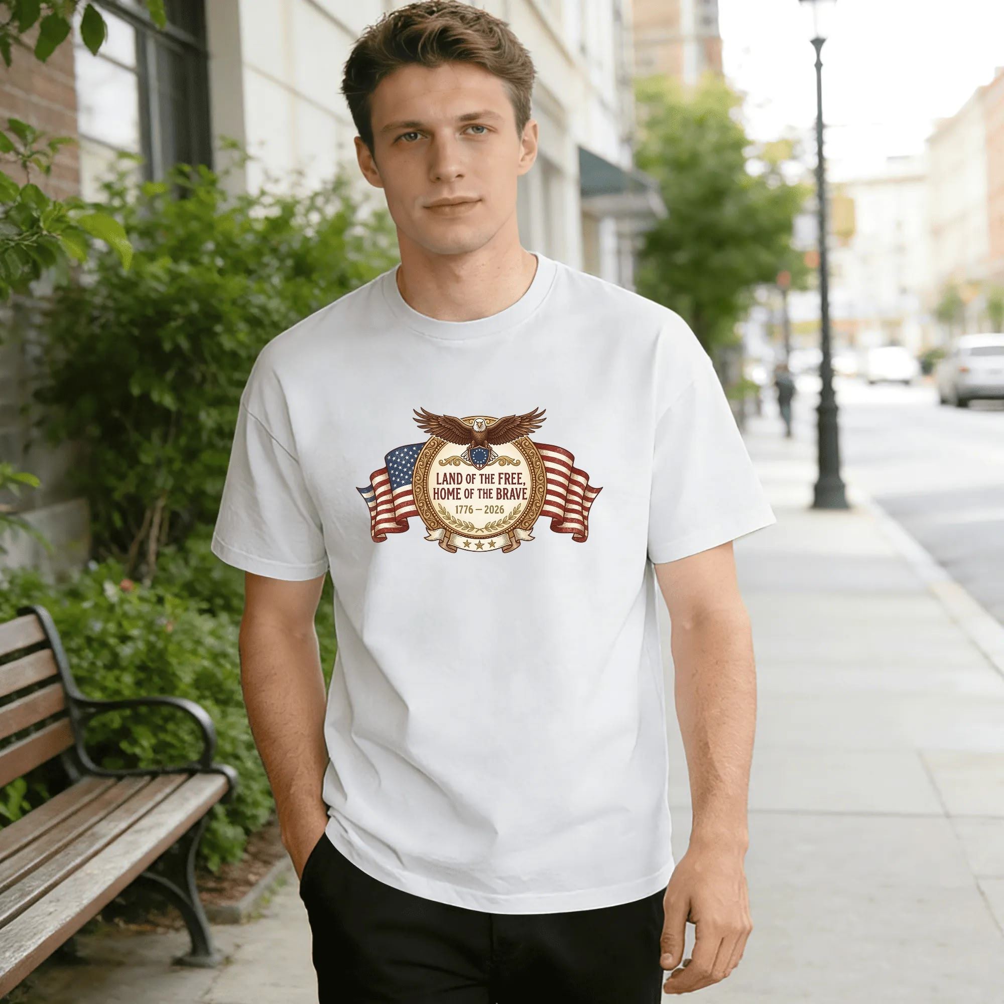 Young man wearing white relaxed‑fit cotton tee with polished vintage circular‑badge America 250 graphic, top spread‑wing bald eagle, draped US flag banner, golden laurel wreath border, “Land of the Free, Home of the Brave” slogan, 1776‑2026 anniversary dates, classic retro patriotic design, street‑style outdoor lifestyle shot, premium USA 250th‑anniversary commemorative apparel