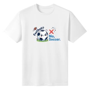 White oversized cotton short‑sleeve t‑shirt, front sweet horizontal cartoon “Football? No, Soccer.” graphic with adorable blushing soccer ball, crossed football, green grass and star sparkle details, casual pro‑soccer sports‑themed tee flat lay