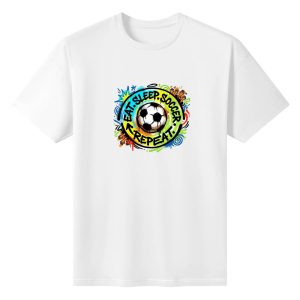 Plain white short‑sleeve crew‑neck t‑shirt featuring bold circular grunge graffiti badge, central traditional soccer ball, curved multicolor “Eat Sleep Soccer Repeat” slogan and playful street‑art decorative elements