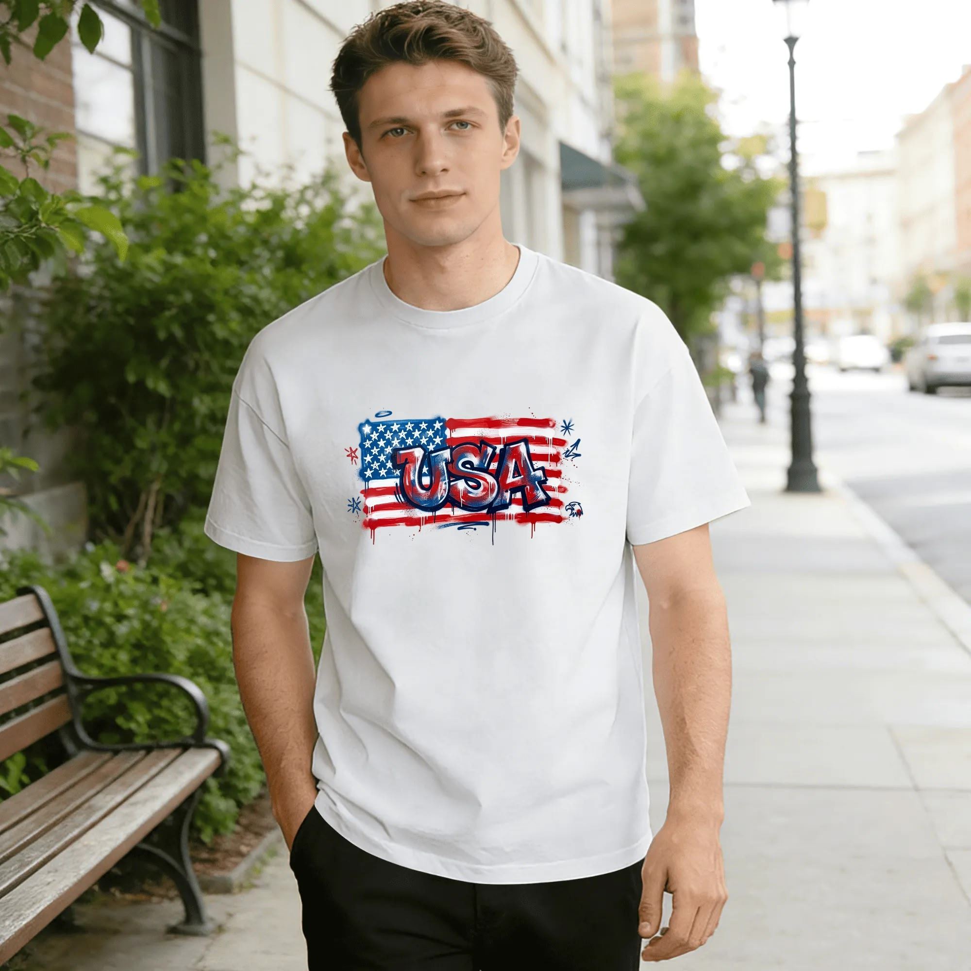Male model on city sidewalk wearing white short-sleeve tee with drip graffiti-style USA & American flag print.