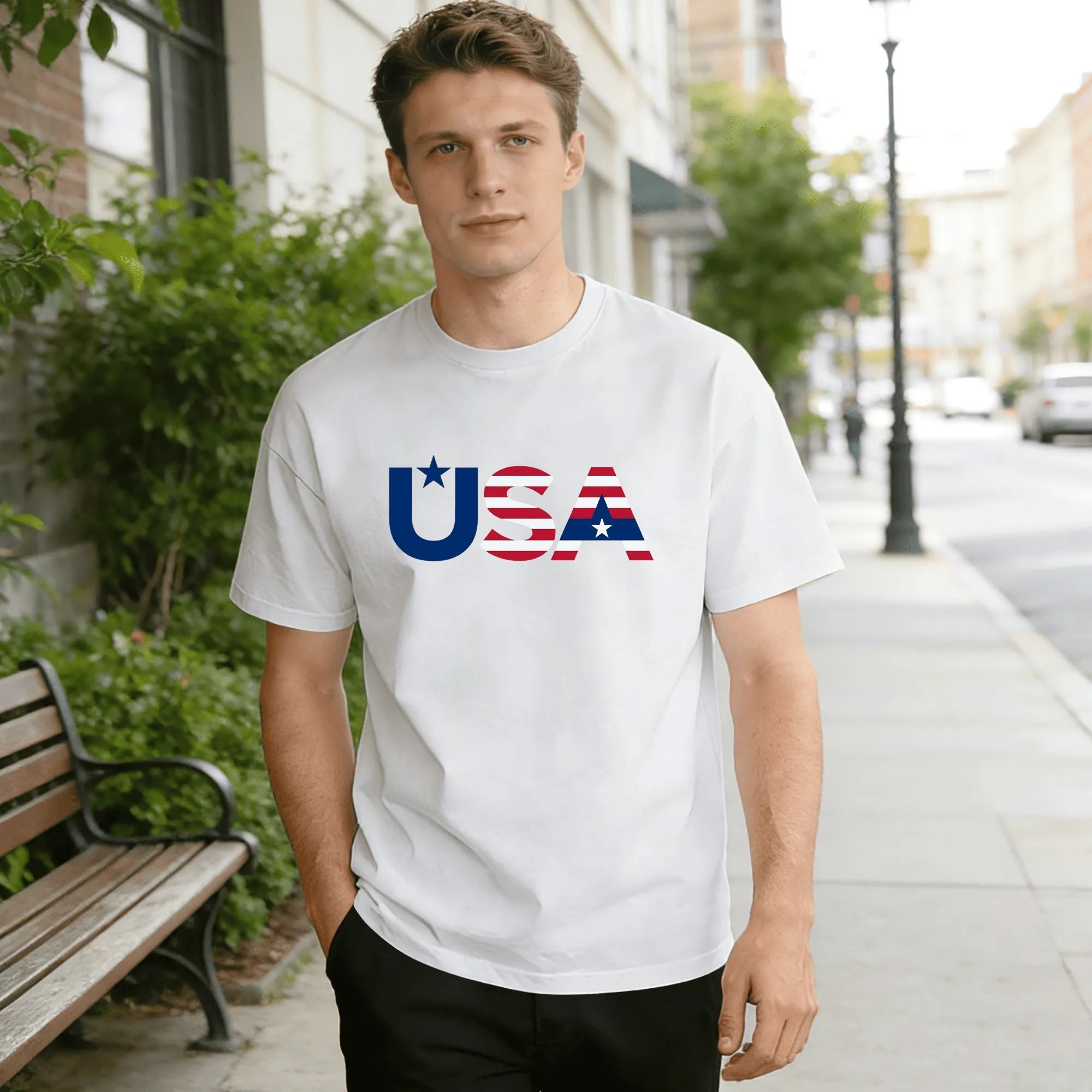 Male model on outdoor sidewalk wearing white short sleeve tee with minimalist star & stripes filled USA letter graphic.