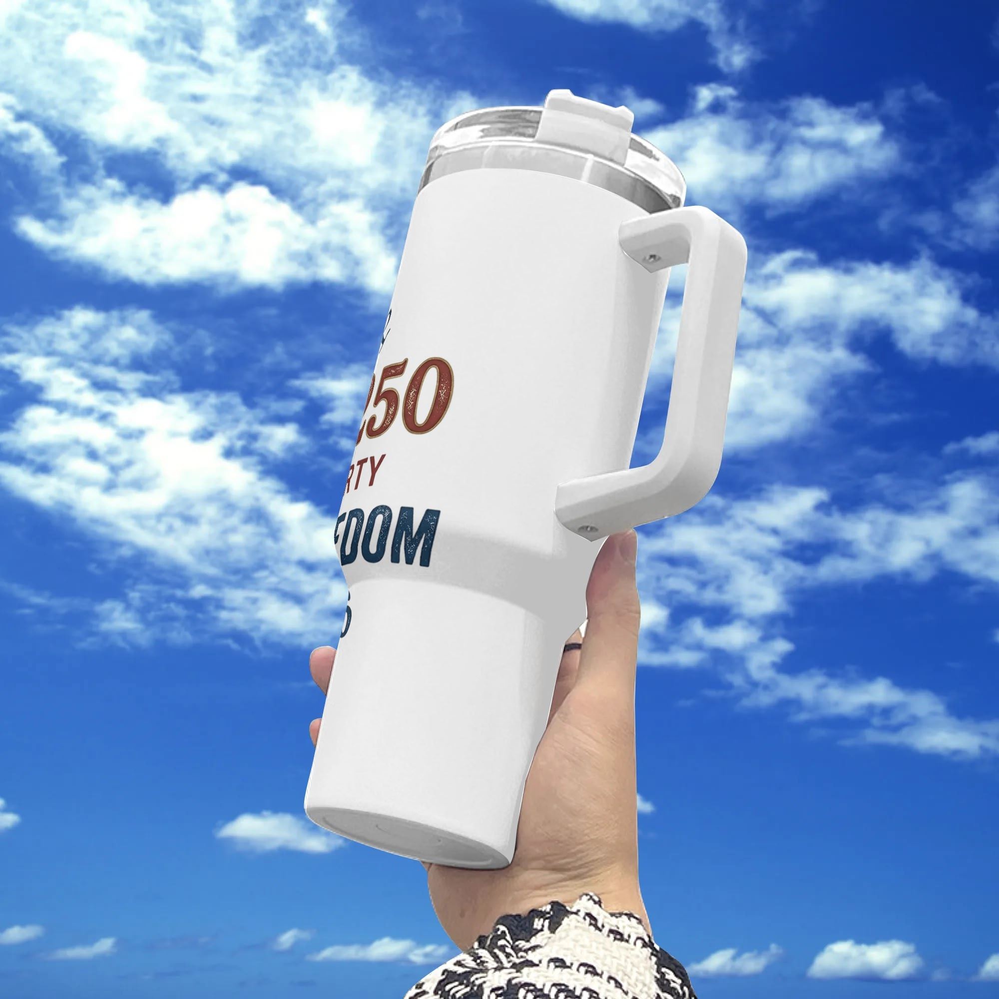Handheld outdoor shot against blue cloudy sky, white 40oz insulated tumbler with vintage multi-color letter print “We The People America 250 Legacy of Liberty Celebrate Freedom 1776-2026”.