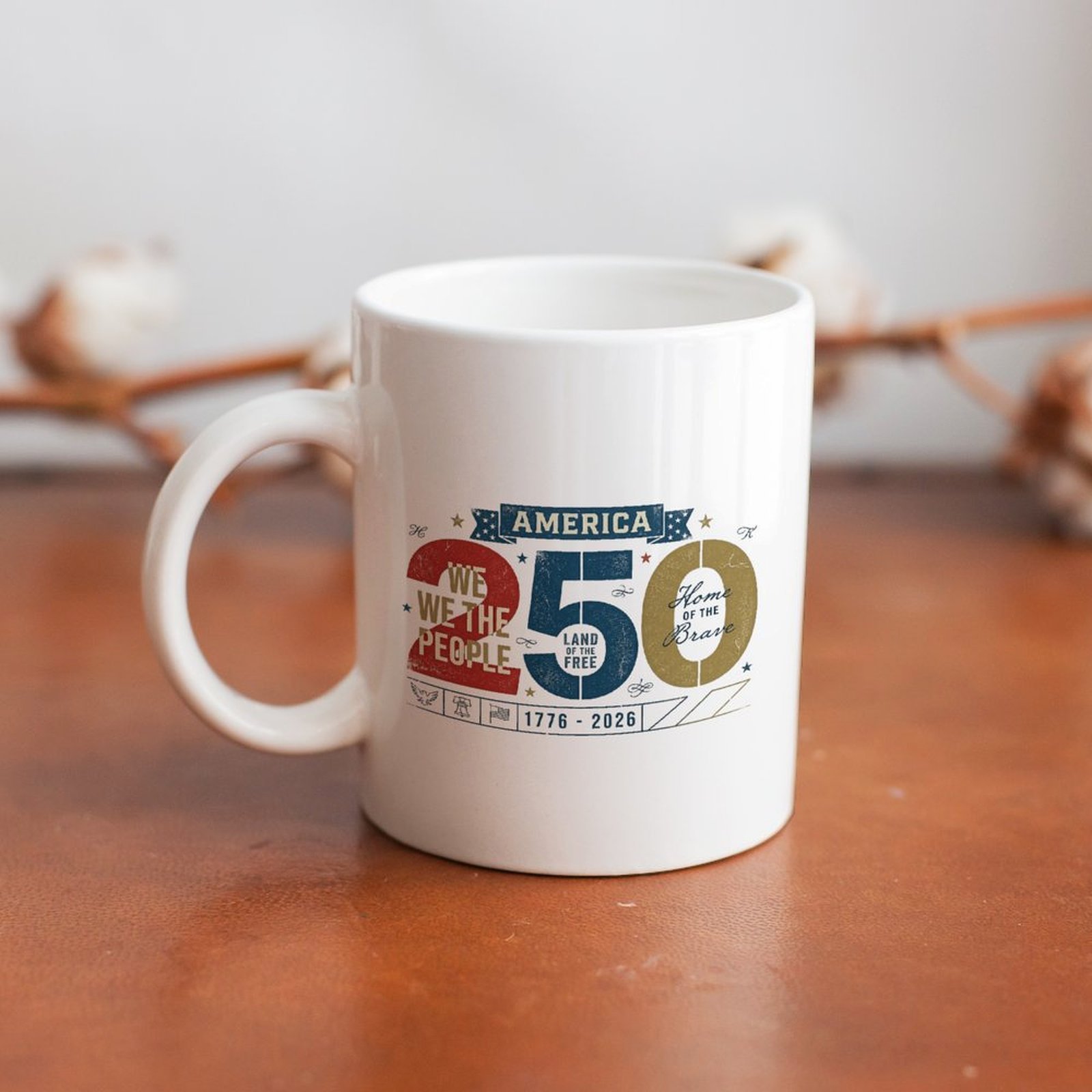 Desk display photo: vintage America 250 graphic white mug placed on warm wood table with dried cotton floral backdrop.