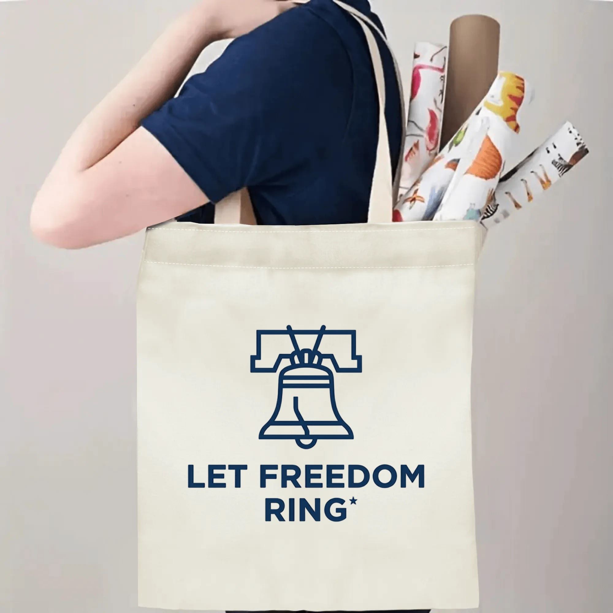 Person carrying navy outline Liberty Bell Let Freedom Ring printed canvas shoulder tote, everyday eco-friendly patriotic carryall bag