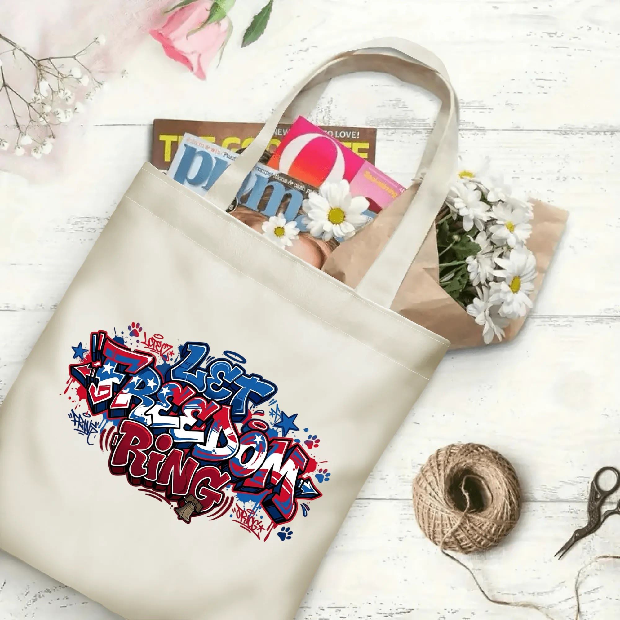Patriotic street art printed canvas shoulder bag laid on rustic wood surface with magazines and fresh daisies
