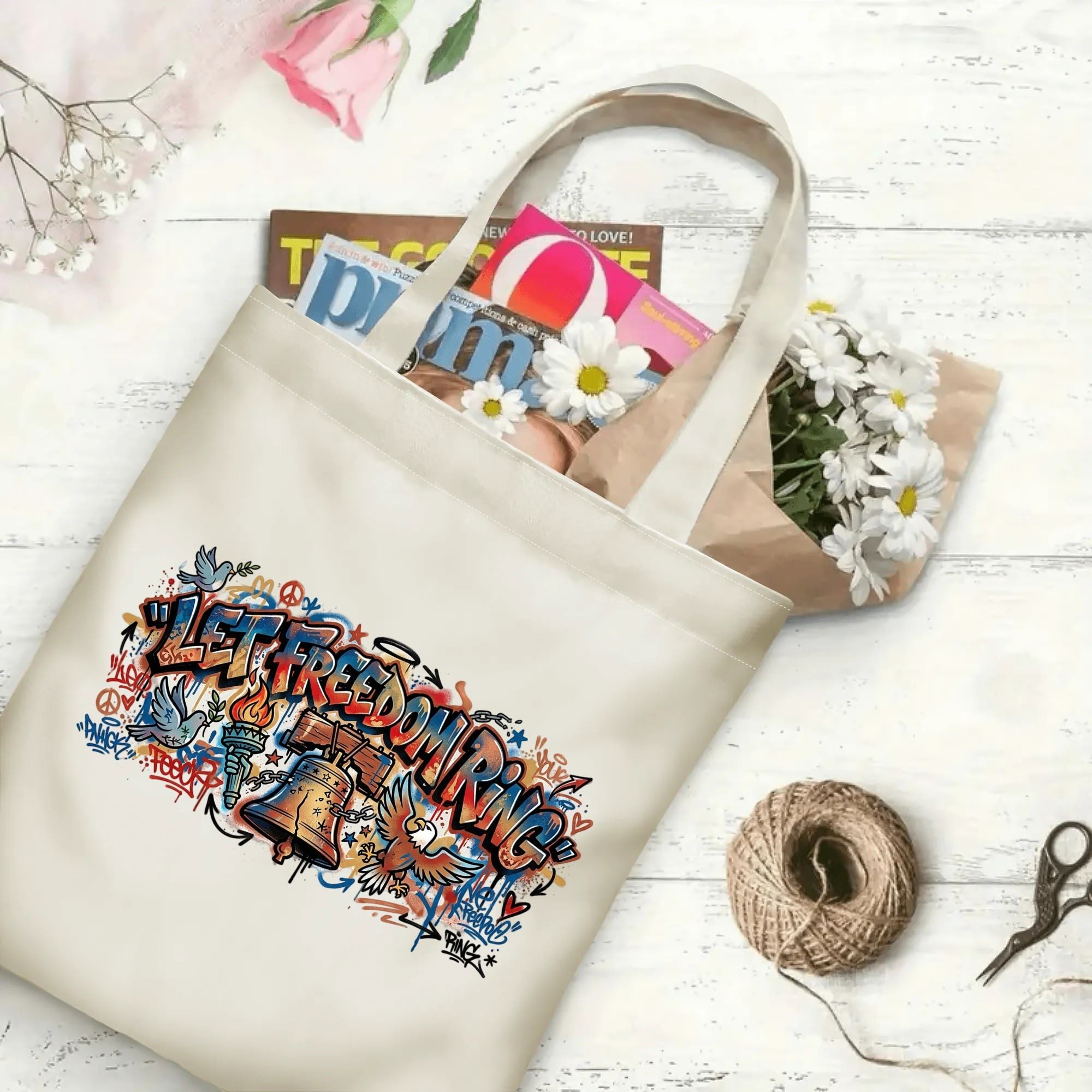 Urban graffiti patriotic print canvas shoulder bag laid on rustic wood surface with magazines and fresh daisy flowers