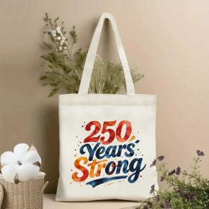 Patriotic tote bag with watercolor-style “250 Years Strong” lettering, styled with dried flowers in a home setting.