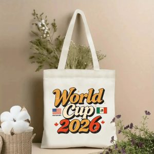Lifestyle shot of the tote bag featuring a retro “World Cup 2026” print, with 70s-style script, host country flags (USA, Mexico) and Canadian maple leaves, displayed against a neutral background with plants.