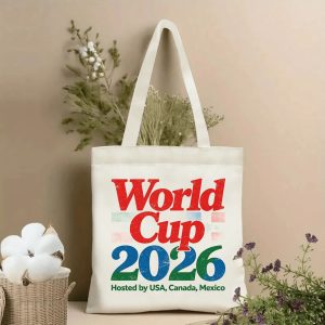 Lifestyle shot of the tote bag featuring a distressed "World Cup 2026" print in red, blue, and green, with the text "Hosted by USA, Canada, Mexico" below, displayed against a neutral background with plants.