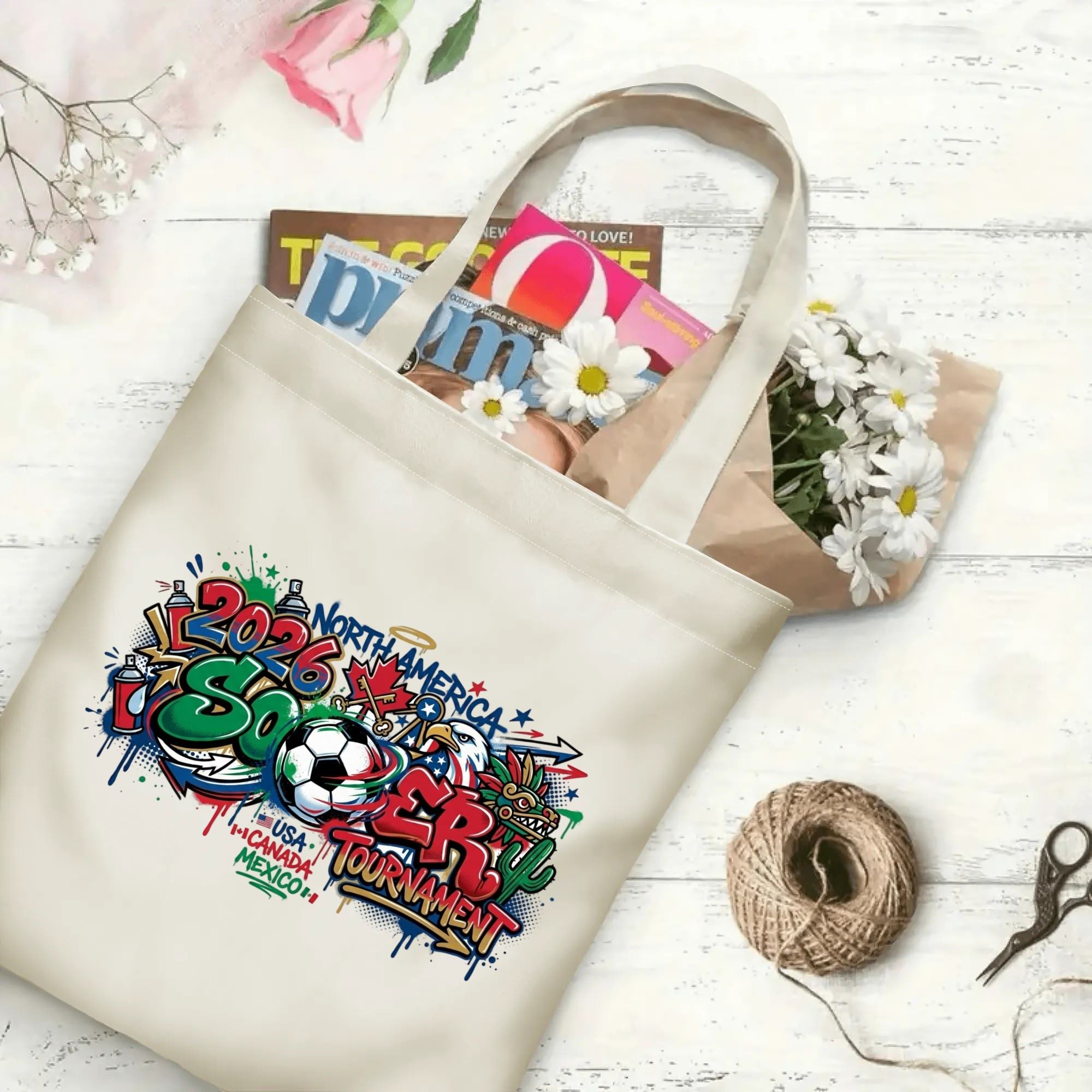 2026 football tournament drip street art canvas tote bag laid flat with magazines, daisies and twine, reusable soccer fan shopping bag